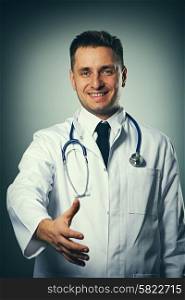 Medical doctor with stethoscope giving hand for handshaking against grey background