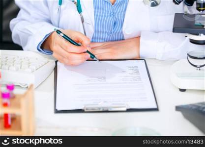 Medical doctor woman sitting at office table and working with document. Close-up&#xA;