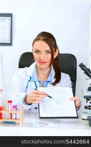 Medical doctor woman sitting at office table with document and pen for signing &#xA;