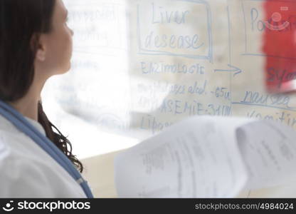 Medical doctor writing patient test results on transparent board to diagnose disease of her patient