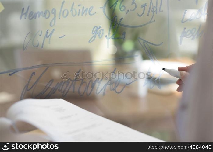 Medical doctor writing patient test results on transparent board to diagnose disease of her patient