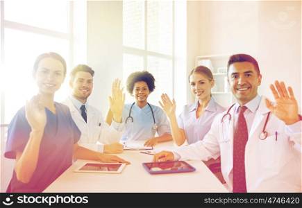medical education, health care, gesture, people and medicine concept - group of happy doctors meeting and waving hands at hospital
