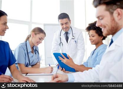 medical education, health care, people and medicine concept - group of happy doctors or interns with mentor meeting and taking notes at hospital