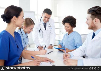 medical education, health care, people and medicine concept - group of happy doctors or interns with mentor meeting and taking notes at hospital