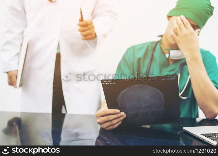 Medical Failure Concept - Surgical doctor covering his face with hand (face palm) expressing disappointment while holding xray film on office desk.