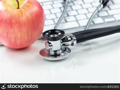 Medical health care concept with traditional stethoscope and apple with computer keyboard in background