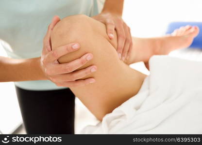 Medical massage at the leg in a physiotherapy center. Female physiotherapist inspecting her patient. Close-up photograph.