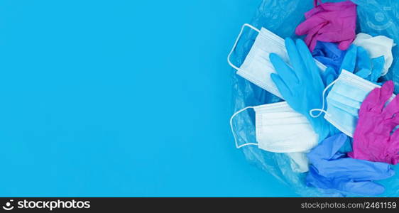 Medical pandemic coronavirus waste, face masks and latex gloves in garbage bag on a blue background with copy space.. Medical pandemic coronavirus waste, face masks and latex gloves in garbage bag on blue background with copy space.