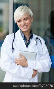 Medical photo of smiling female doctor with stethoscope in front of a glass wall