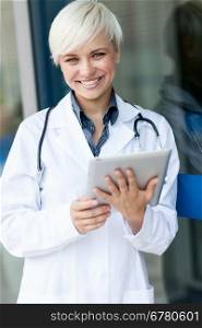 Medical photo of smiling female doctor with stethoscope in front of a glass wall