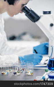 Medical researcher examining a new medicine. Female science student dressed in white lab coat looking through the microscope . Medical Researcher Looking Through the Microscope