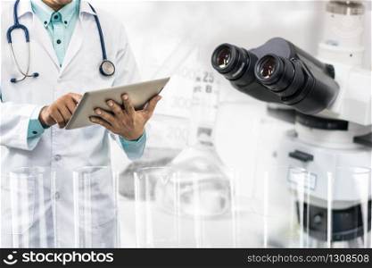 Medical science research and development concept - Doctor holding tablet computer with scientific instrument, microscope and chemical test tube in lab background.