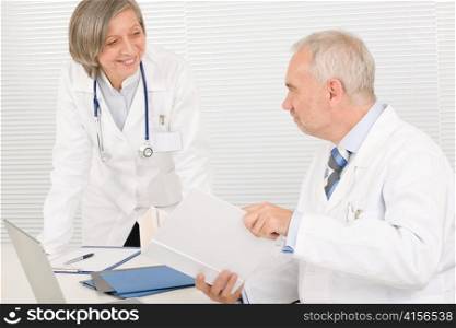 Medical senior doctor male reading book with professional female colleague