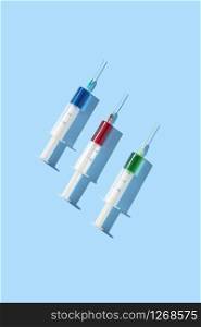Medical set of sterile plastic disposable syrenges 20 ml with colorful vaccines or serum for an intravenous injection on a pastel blue background with hard shadow, copy space. Top view.. Therapeutic set of plastic syrenges with colorful vaccines.