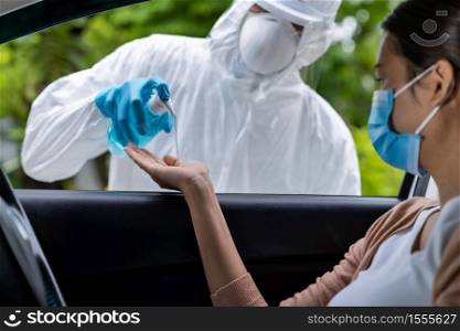 Medical staff give alcohol gel hand sanitiser to asian woman before coronavirus covid-19 test at drive thru station in hospital. New normal healthcare drive thru service and medical concept.