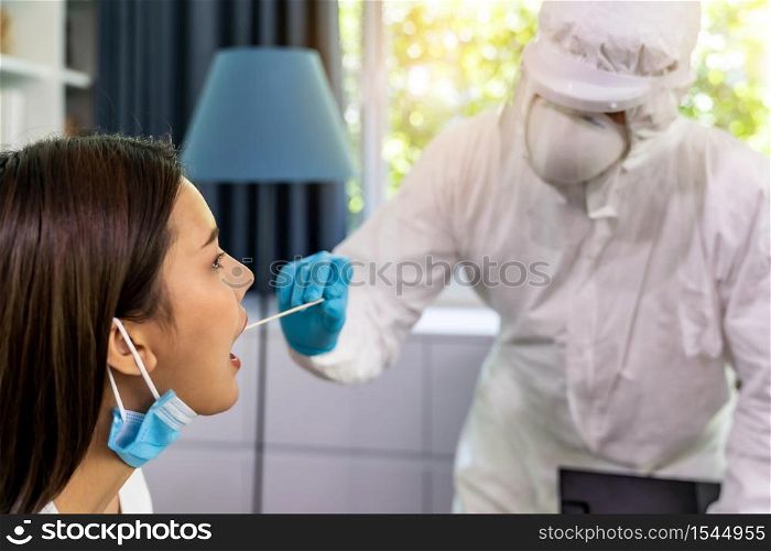 Medical staff with PPE suit test coronavirus covid-19 to asian woman by throat swab at home. New normal healthcare service at home and medical delivery concept.