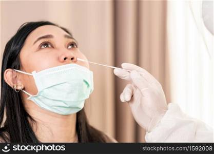 Medical staff with PPE suit test coronavirus covid-19 to asian woman by nose swab at hospital. COVID-19 testing health care concept.