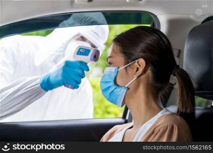 Medical staff with PPE Take Temperature for fever to asian woman before coronavirus covid-19 test at drive thru station in hospital. New normal healthcare drive thru service and medical concept.