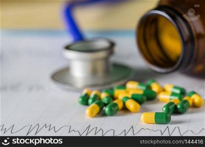 Medical stethoscope head lying on cardiogram chart with pile of pills closeup. Cardiology care, health, protection, prevention and help. Healthy life or insurance concept