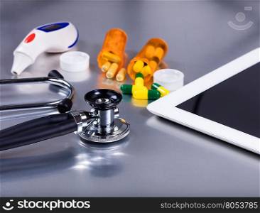 Medical stethoscope on exam table with medicine pills, thermometer, bottles and mobile computer. Selective focus on stethoscope.