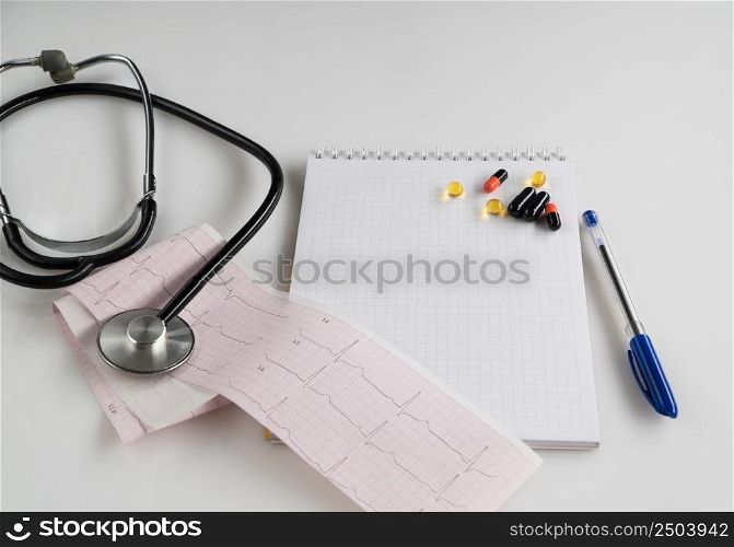medical stethoscope with pills and tonometer on white surface. medical prescription. stethoscope with cardiogram