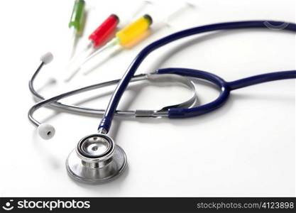Medical still photo with blue stethoscope and colorful syringe over white