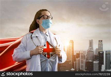 Medical superhero showing flag of UK. Heroic doctor wearing mask and red cape fighting with epidemic in city. Young woman. Brave medical staff concept.. Heroic doctor fighting with epidemic