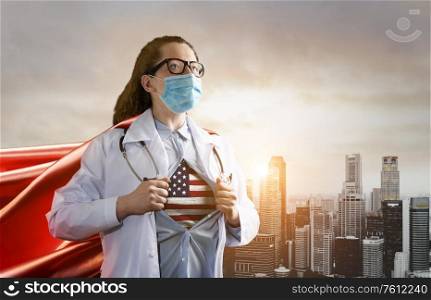 Medical superhero showing flag of USA. Heroic doctor wearing mask and red cape fighting with epidemic in city. Young woman. Brave medical staff concept.. Heroic doctor fighting with epidemic