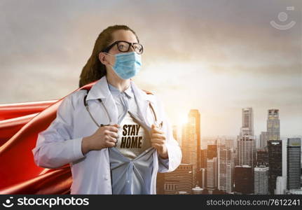 Medical superhero showing stay home caption. Heroic doctor wearing mask and red cape fighting with epidemic in city and promoting stayhome movement. Young woman. Brave medical staff concept.. Heroic doctor fighting with epidemic