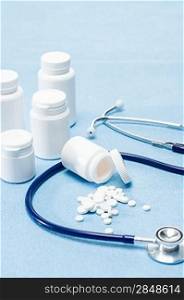 Medical supplies spilled tablets and stethoscope on blue background