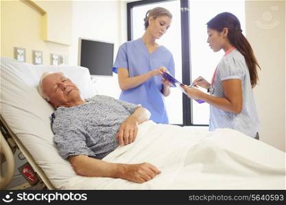 Medical Team Meeting As Senior Man Sleeps In Hospital Room