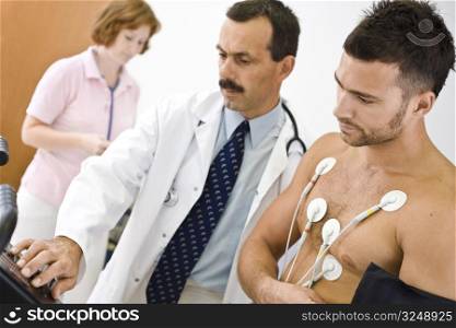 Medical team performing an EKG test on young male patient. Real people, real locacion, not a staged photo with models. Focus is placed on the patient.