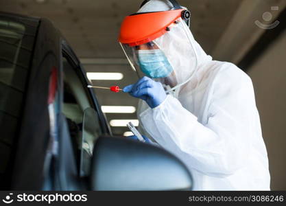 Medical worker in personal protective equipment swabbing a person in a car drive through Coronavirus COVID-19 mobile testing center,oral and nasal specimen collection procedure,health and safety
