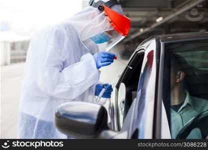 Medical worker in PPE performing nasal & throat swab on person in vehicle through car window,COVID-19 mobile testing centre,drive through facility parking lot,specimen collection and rt-PCR diagnostic