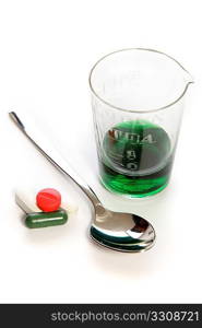 Medication - pills and a green medicine in an old glass measuring cylinder, with a teaspoon