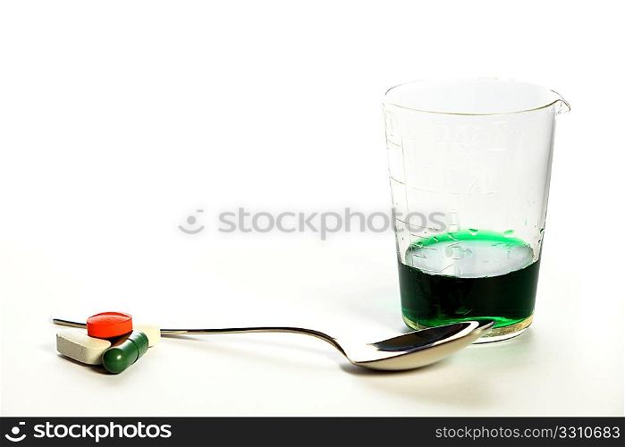 Medication - pills and a green medicine in an old glass measuring cylinder, with a teaspoon