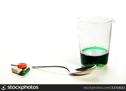 Medication - pills and a green medicine in an old glass measuring cylinder, with a teaspoon