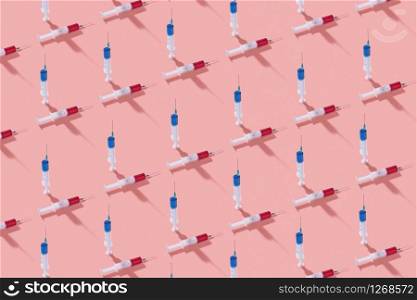 Medicinal horizontal pattern from disposable vertical and horizontal plastic syringes with red and blue vaccine and serum for injection on a living coral background, shadows.. Medicinal pattern with vertical and horizontal plastic syringes.