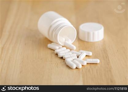 Medicinal plastic bottle and white pills on a wooden table. Medicinal bottle and white drugs on a wooden table