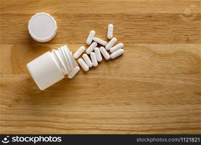 Medicinal plastic bottle and white pills on a wooden table. Medicinal bottle and white drugs on a wooden table