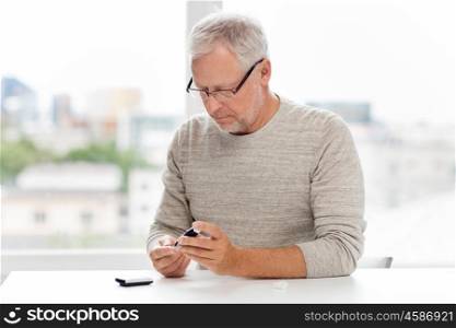 medicine, age, diabetes, health care and old people concept - senior man with glucometer checking blood sugar level at home