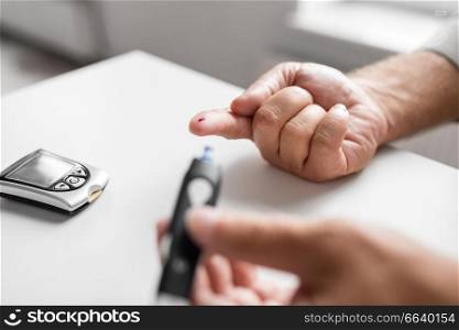 medicine, age, diabetes, health care and old people concept - senior man with glucometer checking blood sugar level at home. senior man with glucometer checking blood sugar