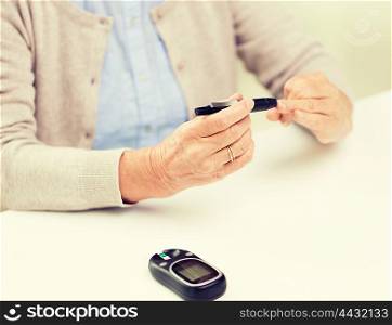 medicine, age, diabetes, health care and people concept - close up of senior woman with glucometer checking blood sugar level at home
