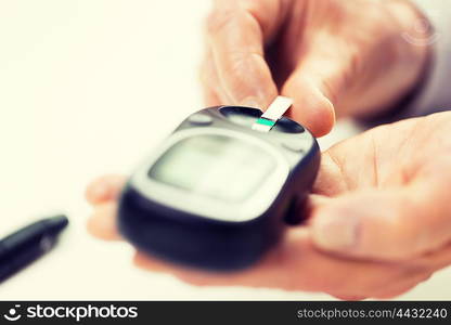 medicine, age, diabetes, health care and people concept - close up of senior woman with glucometer and test stripe checking blood sugar level at home