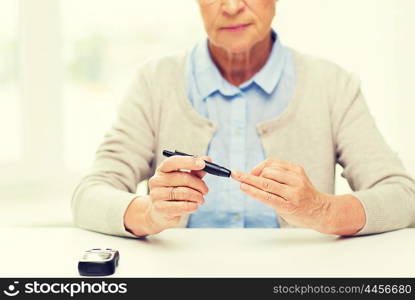 medicine, age, diabetes, health care and people concept - close up of senior woman with glucometer checking blood sugar level at home