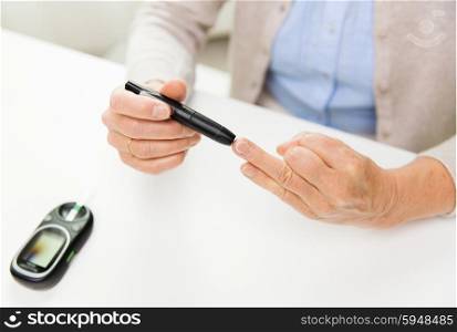 medicine, age, diabetes, health care and people concept - close up of senior woman with glucometer checking blood sugar level at home