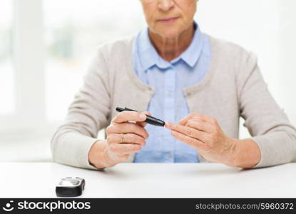 medicine, age, diabetes, health care and people concept - close up of senior woman with glucometer checking blood sugar level at home