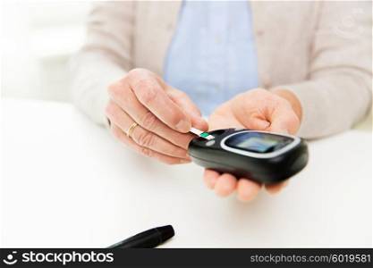 medicine, age, diabetes, health care and people concept - close up of senior woman with glucometer and test stripe checking blood sugar level at home
