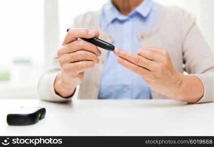 medicine, age, diabetes, health care and people concept - close up of senior woman with glucometer checking blood sugar level at home