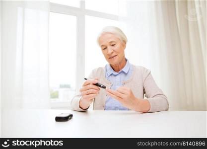 medicine, age, diabetes, health care and people concept - happy senior woman with glucometer checking blood sugar level at home